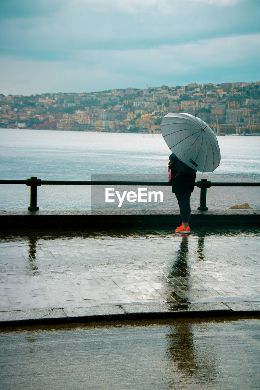 Rear view of woman standing on footpath against sea