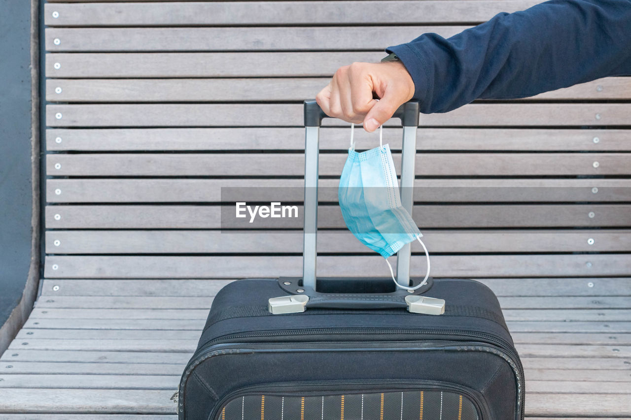 Cropped hand of man holding mask and suitcase