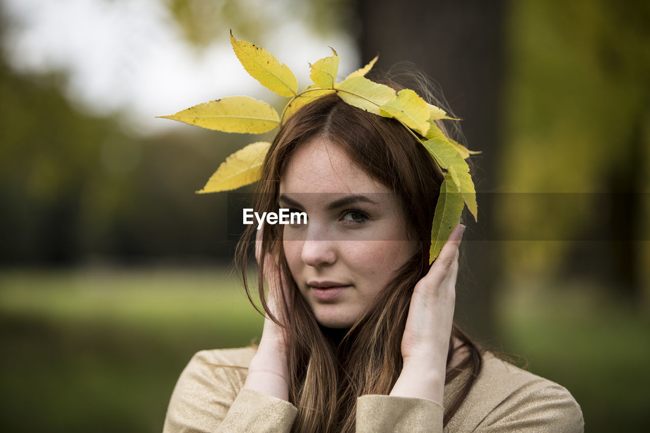 Close-up portrait of beautiful young woman holding leaf crown