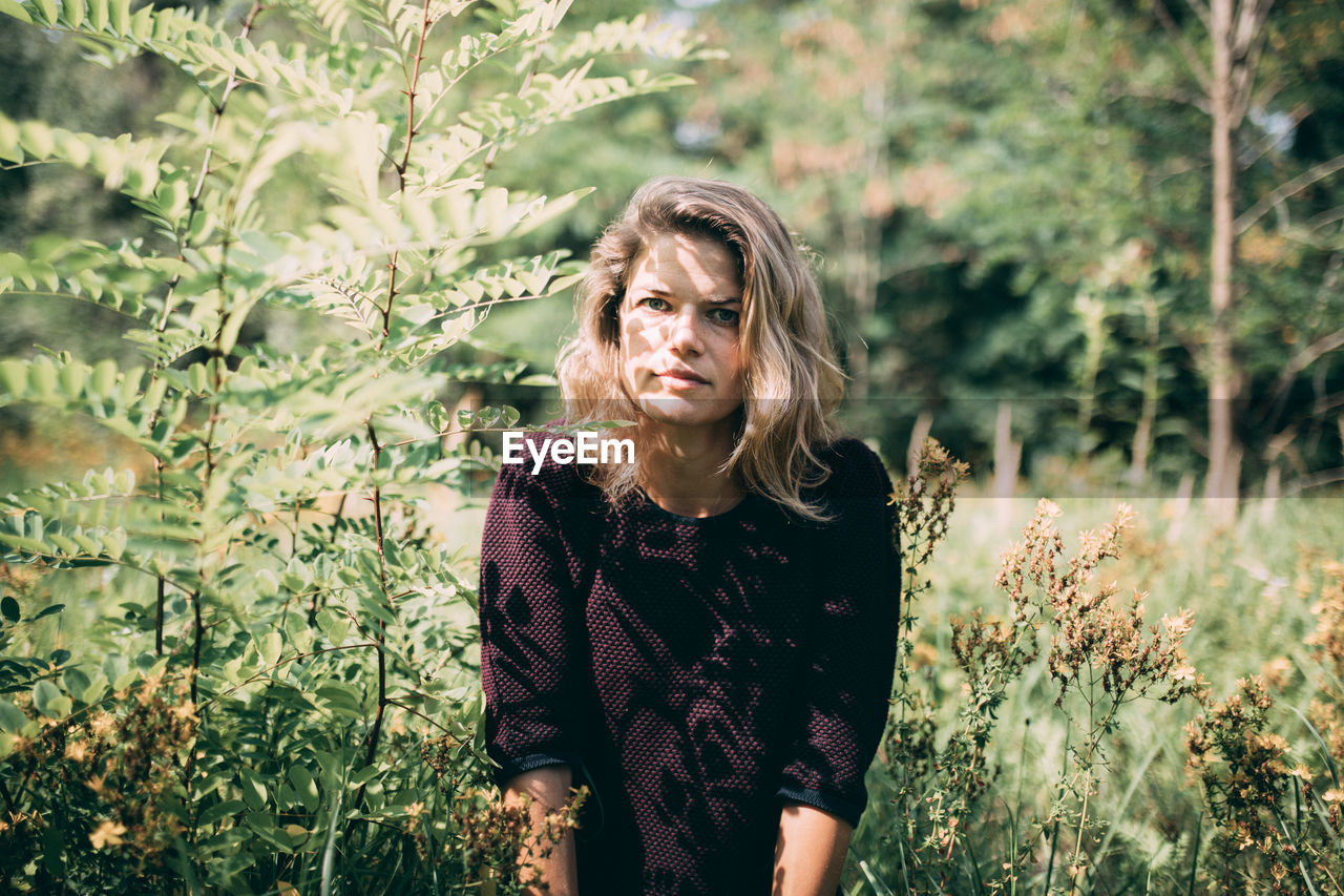 Portrait of woman standing amidst plants in forest