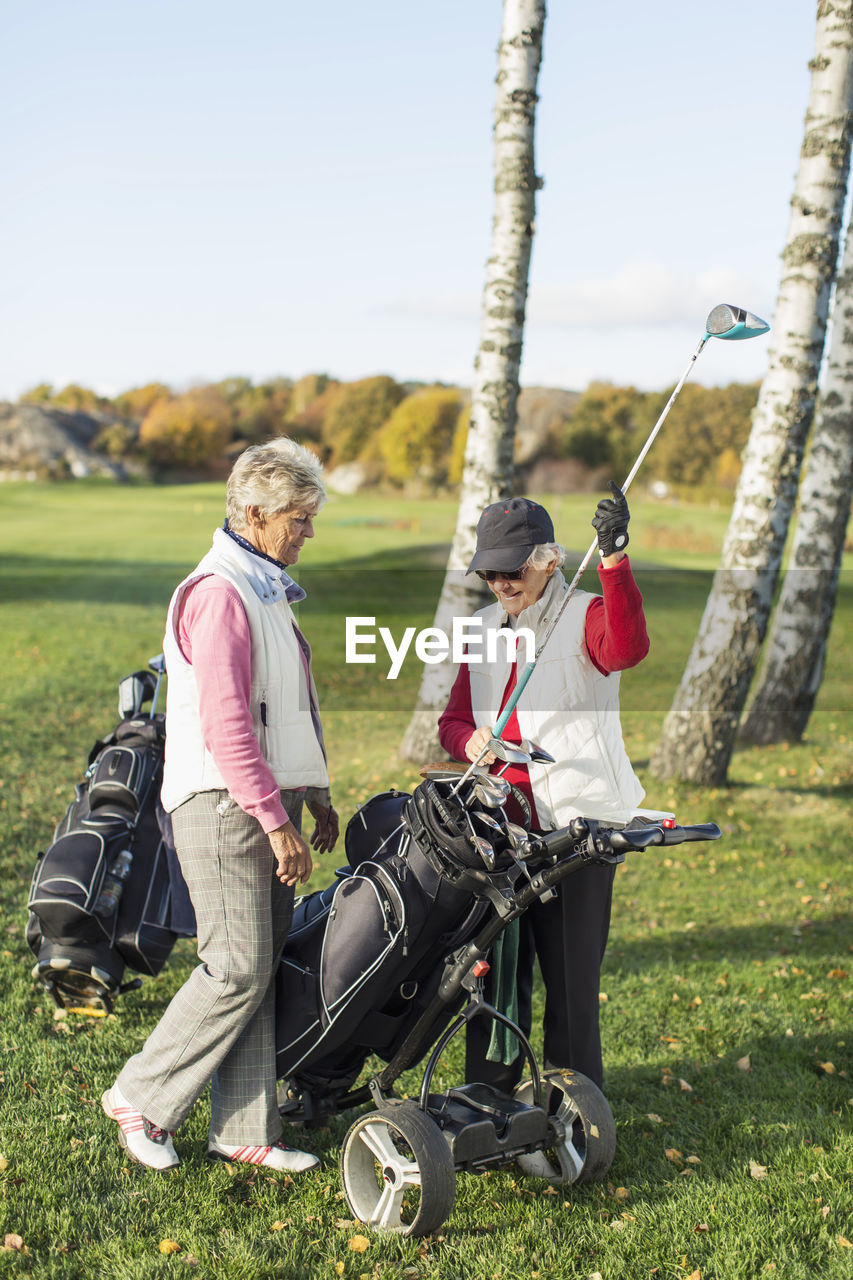 Full length of senior female friends choosing golf club on golf course