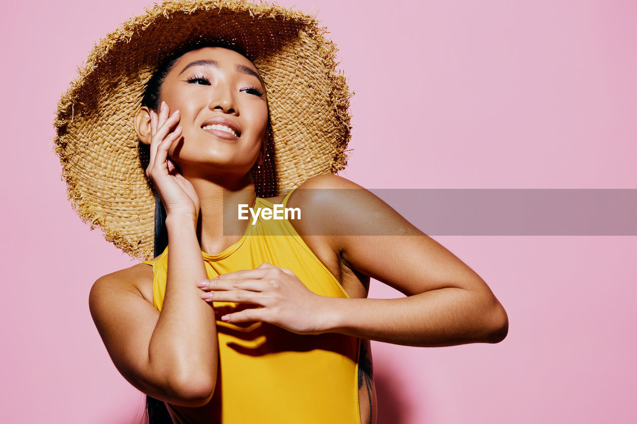 portrait of smiling young woman wearing hat against pink background