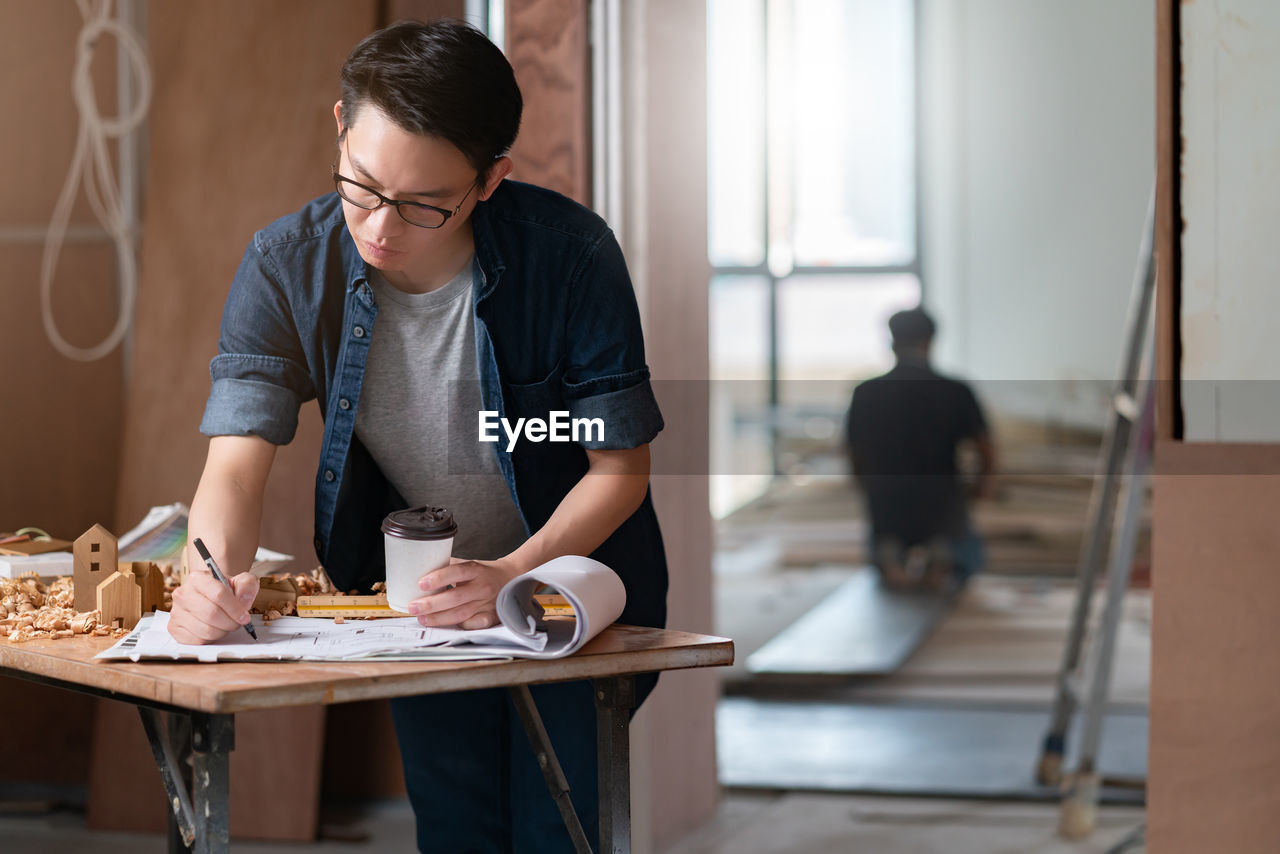 Mid adult man holding coffee drawing on paper while standing in house