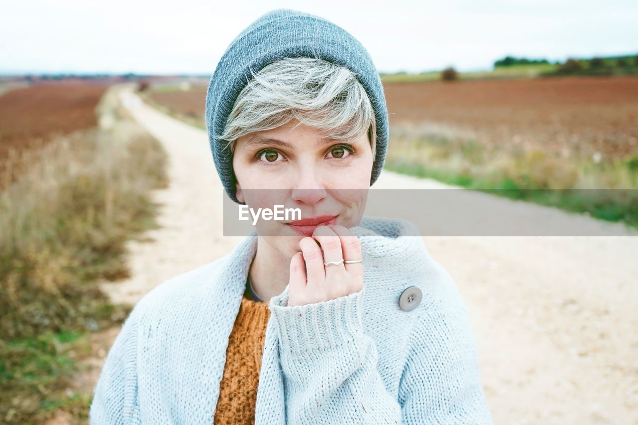 Close-up portrait of woman wearing knit hat while standing on dirt road