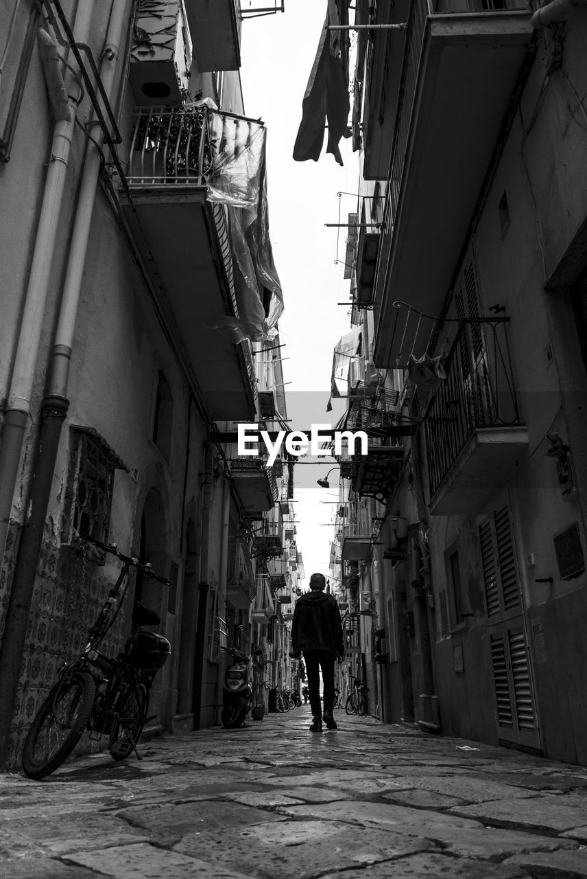 Rear view of man walking on street amidst buildings