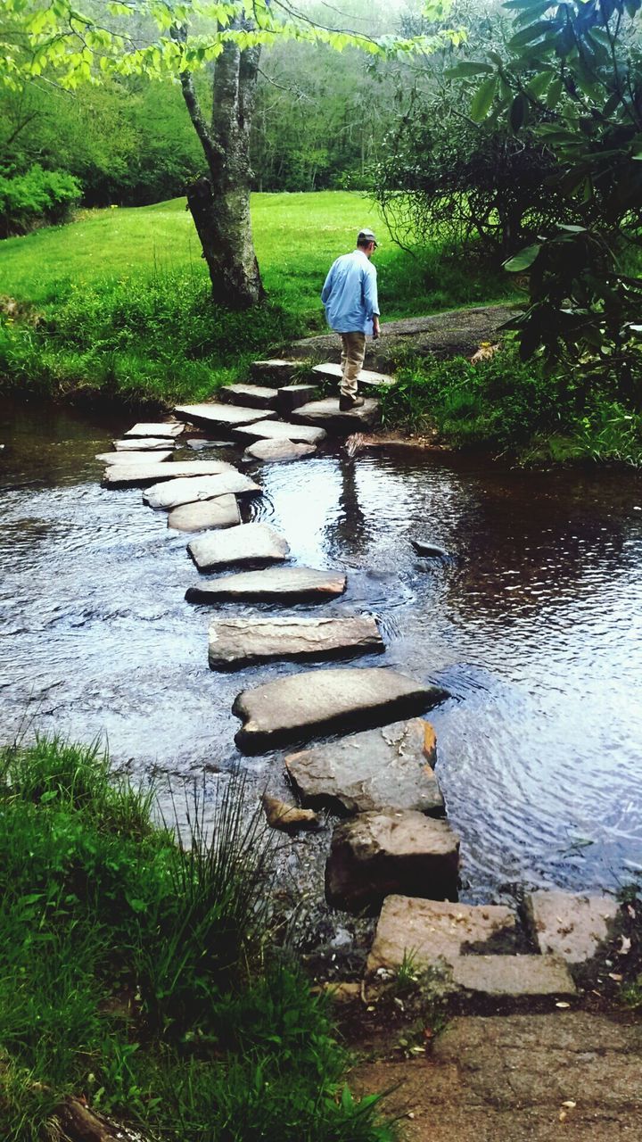 Rear view of man walking on stepping stones