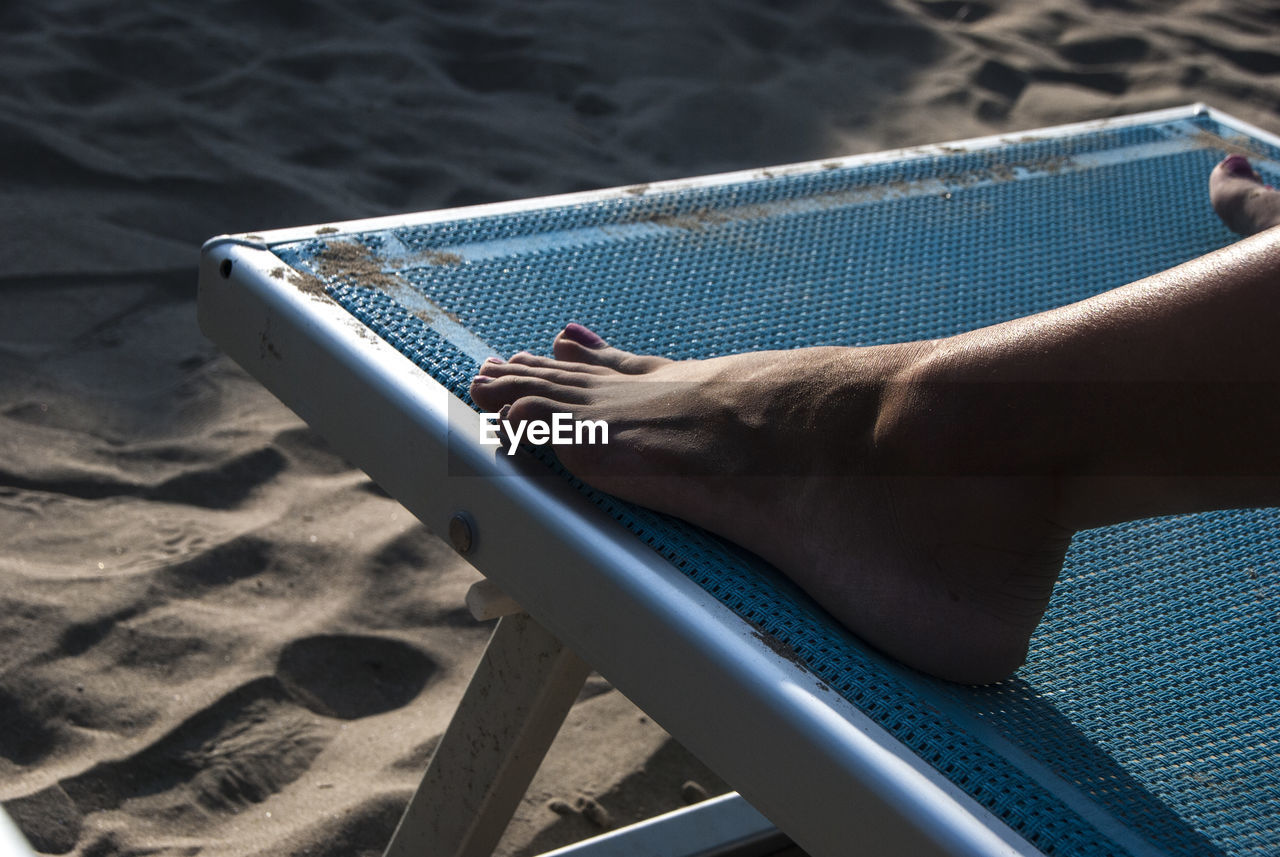 Low section of woman relaxing on deck chair at beach