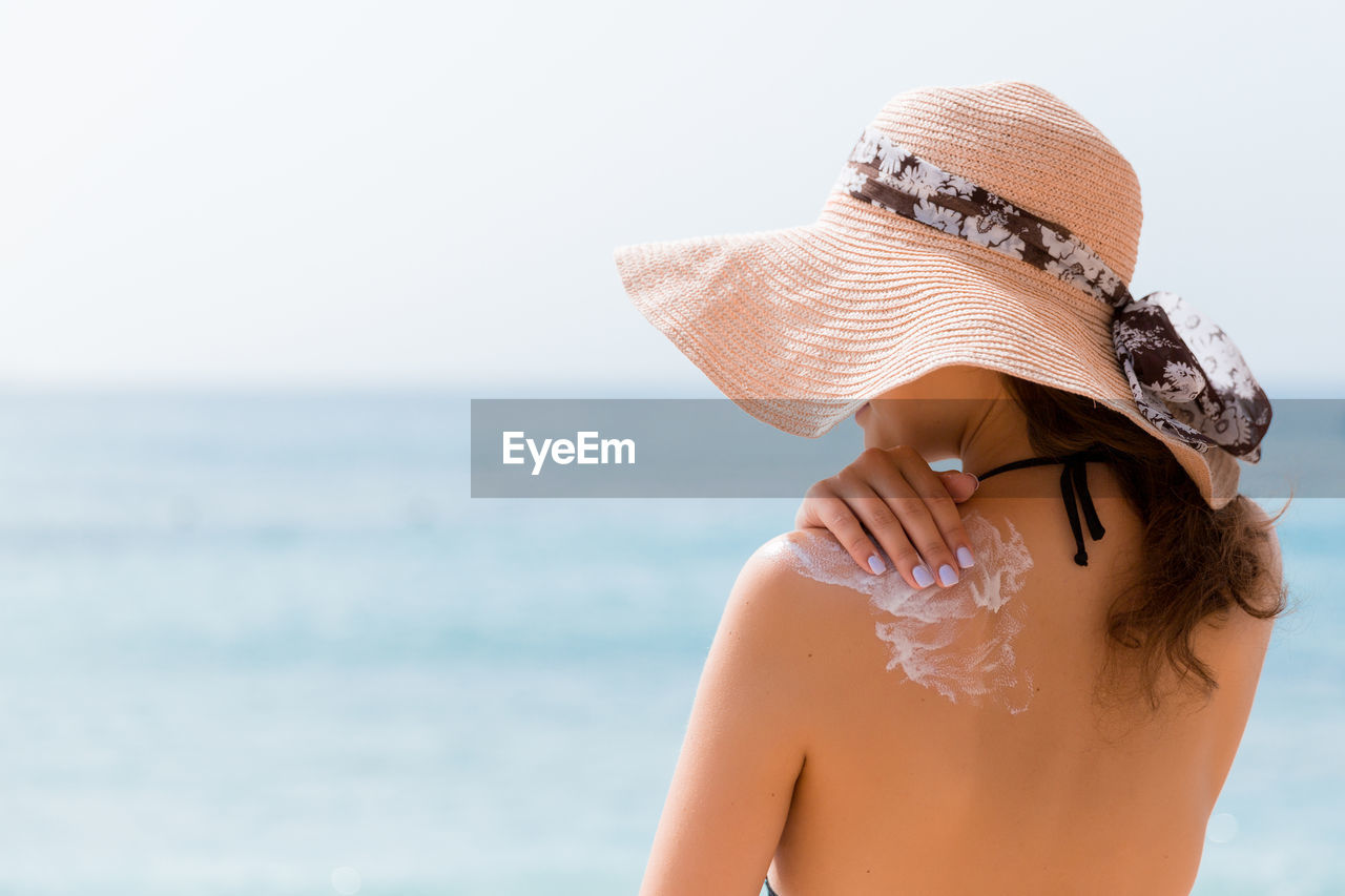 REAR VIEW OF WOMAN WITH HAT ON BEACH