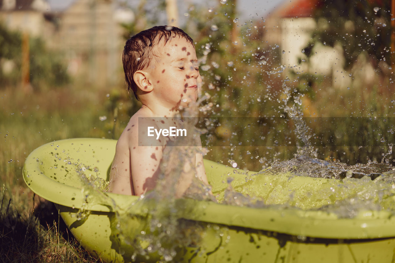 Cute little boy bathing in tub outdoors in garden. happy child is splashing, playing with water