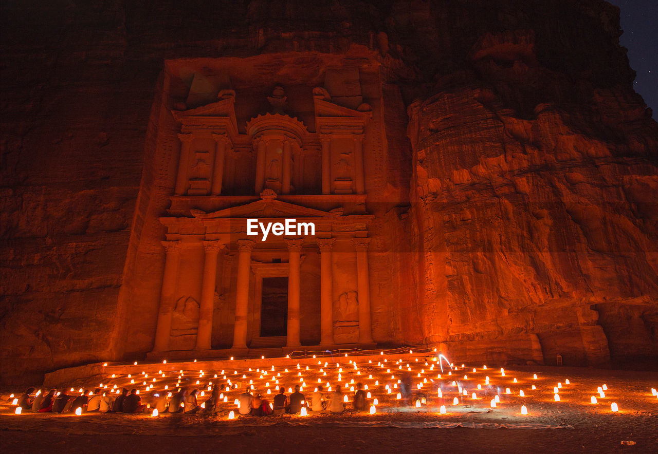 Low angle view of people sitting against illuminated building at night