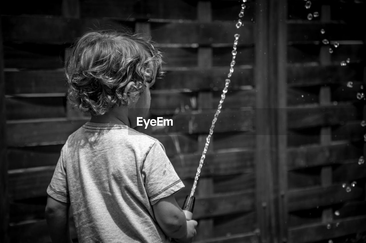 Rear view of boy spraying water outdoors