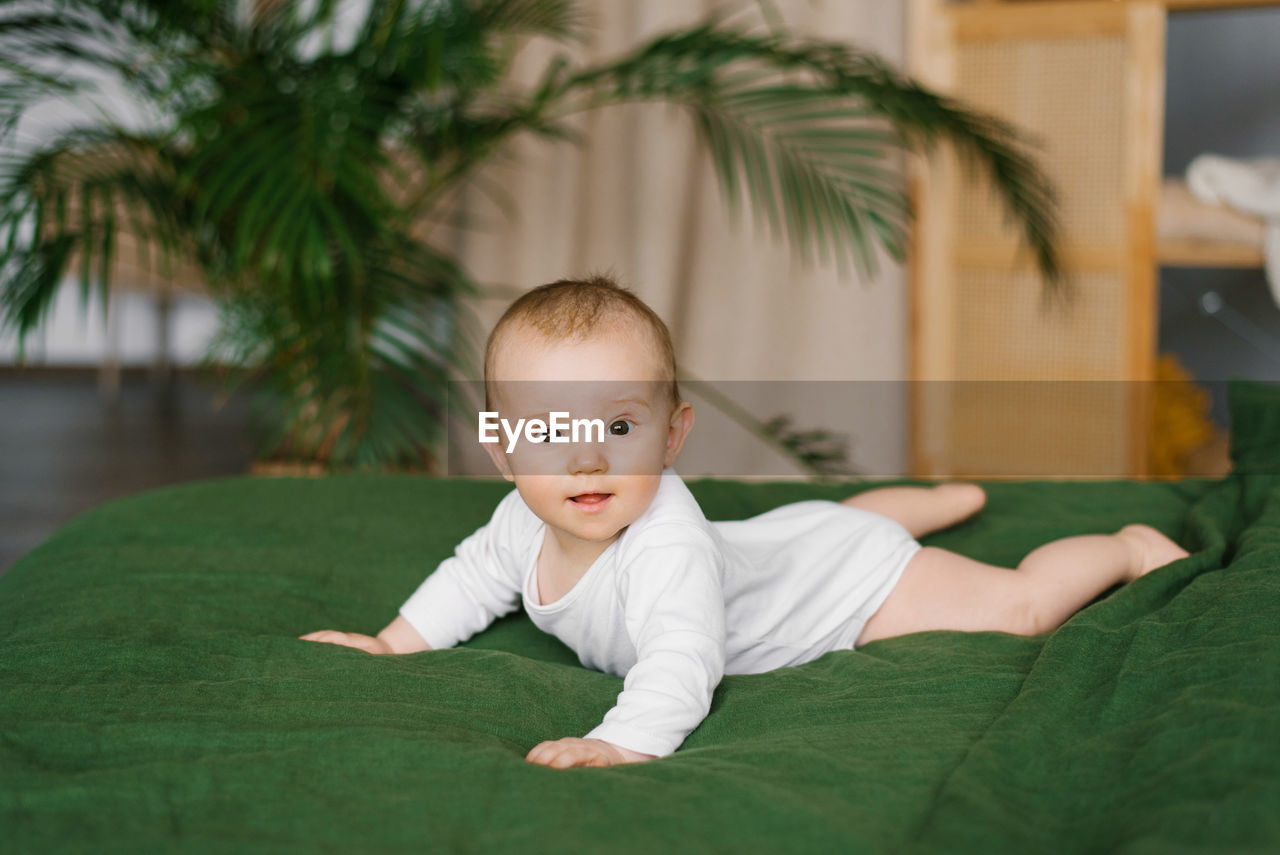 Small beautiful child lies on the bed on his stomach and smiles. happy toddler boy