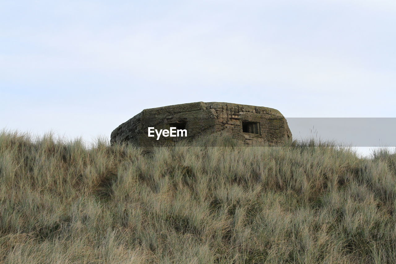 Low angle view of abandoned pill box on grassy field