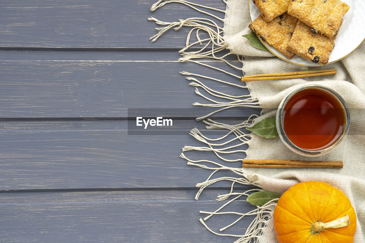 Autumn flatlay with pumpkin, cookies, clay cup with tea and cinnamon chopsticks on gray background. 