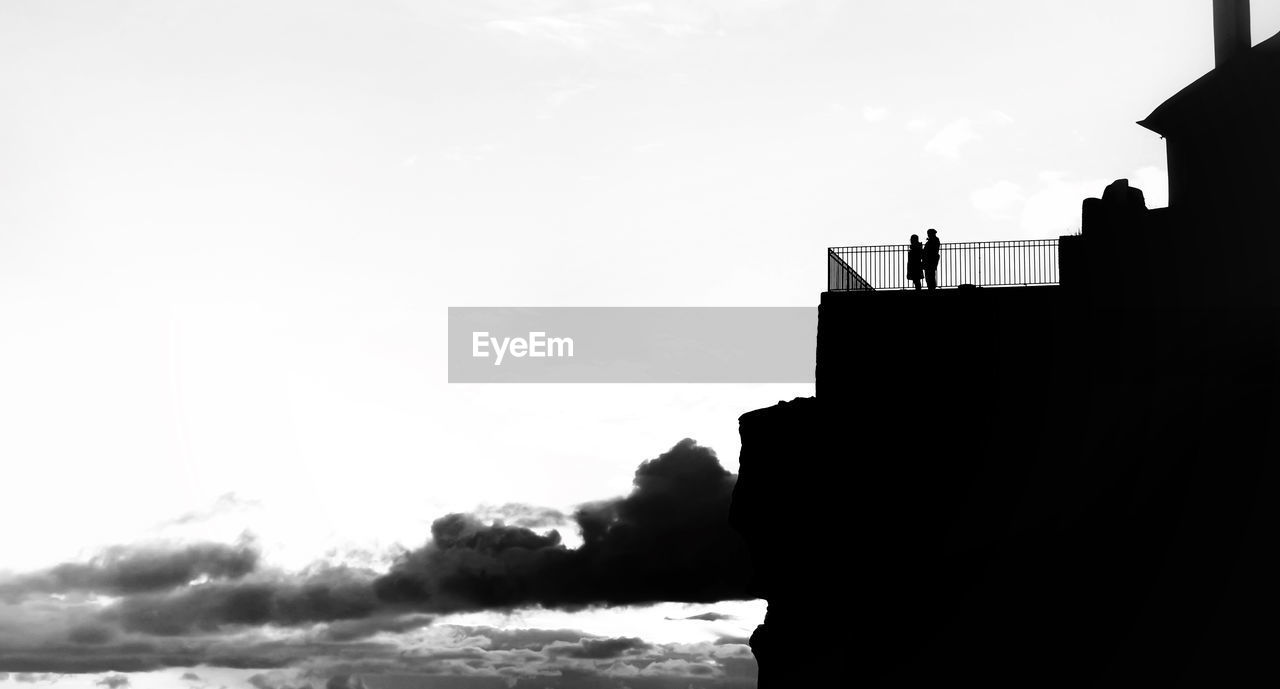 Low angle view of silhouette people standing on building against sky