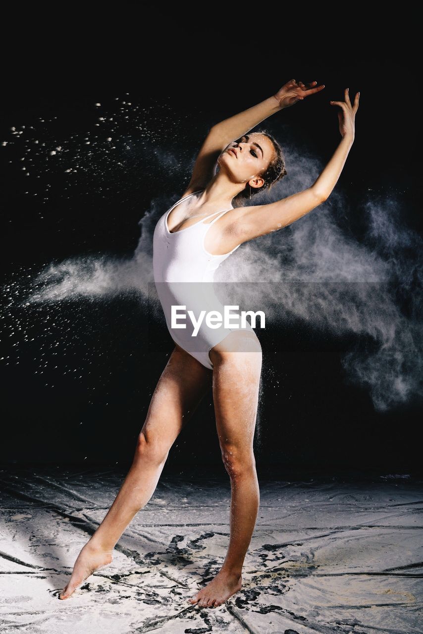 Young woman dancing with chalk powder against black background