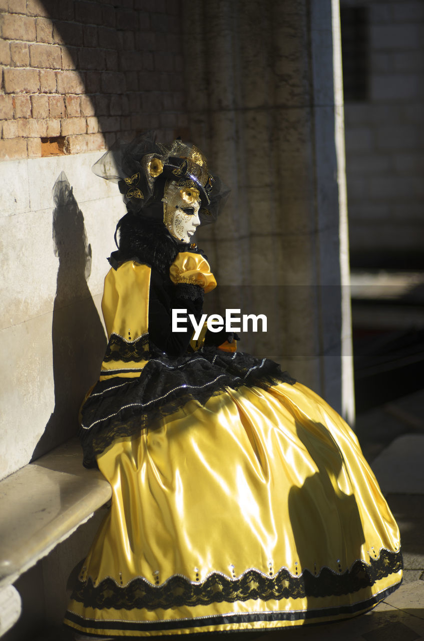 Woman wearing mask and costume sitting on bench during carnival of venice