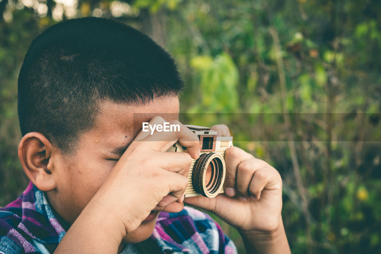 Close-up of boy photographing through camera against plants