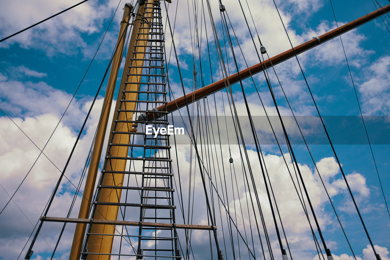 Sailing mast with ropes in front of cloudy blue sky