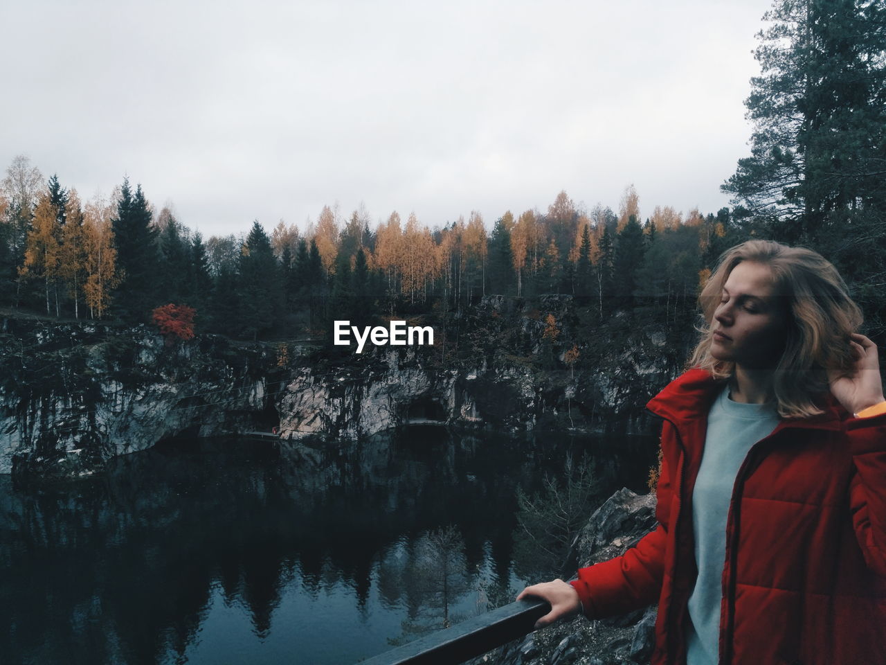 Young woman with eyes closed standing by lake in forest during autumn