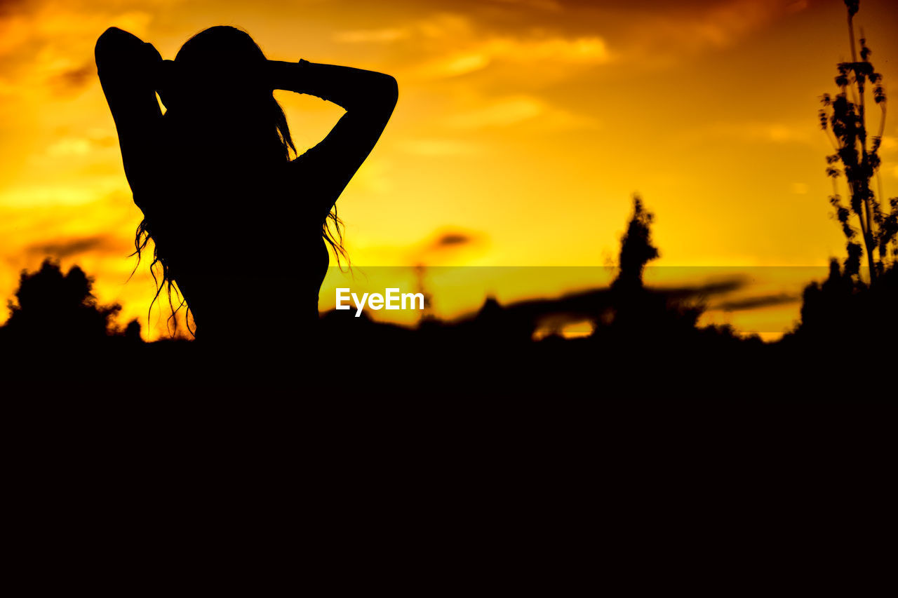 Silhouette woman standing against an orange sky