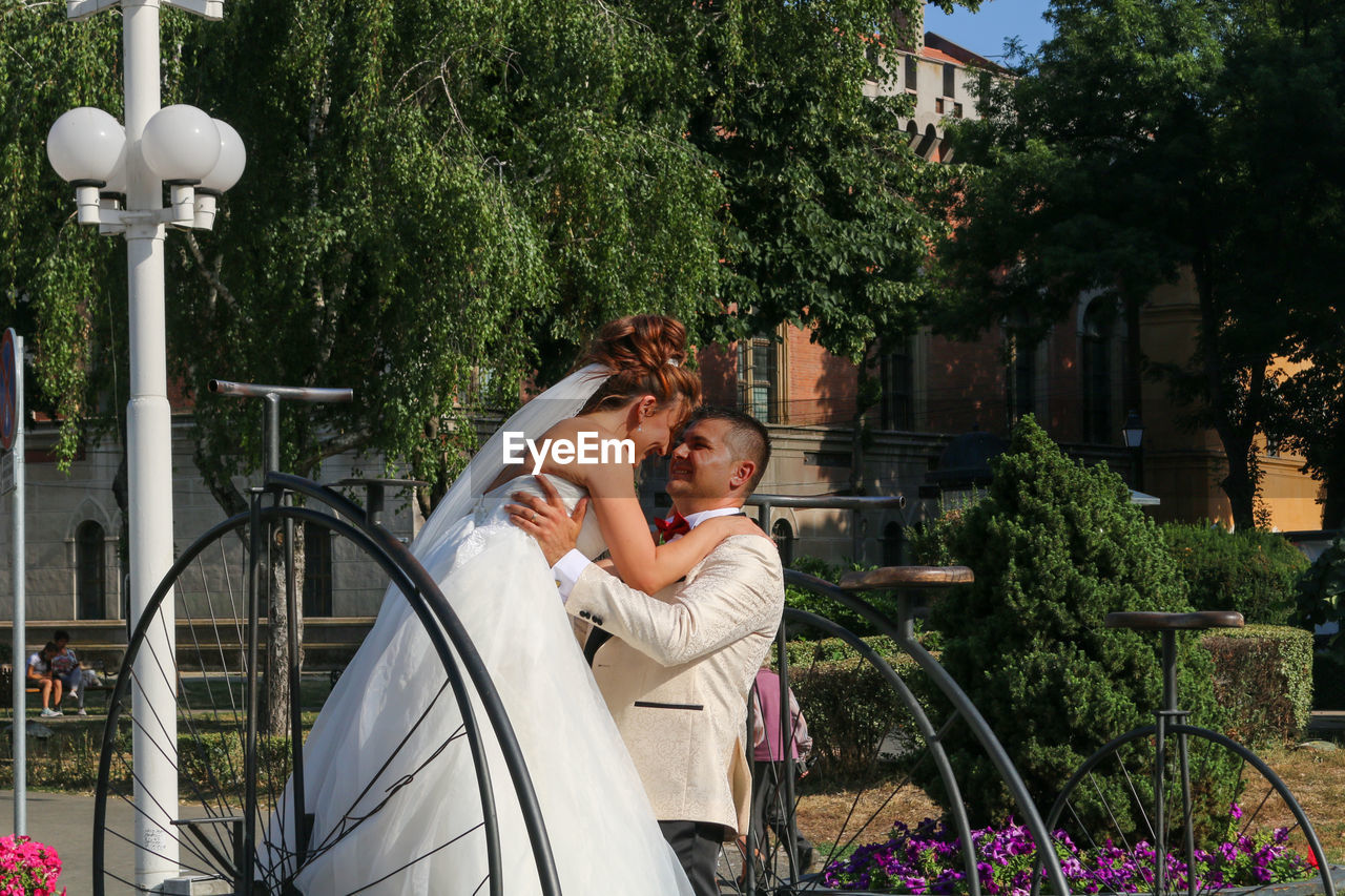 Groom carrying bride against trees