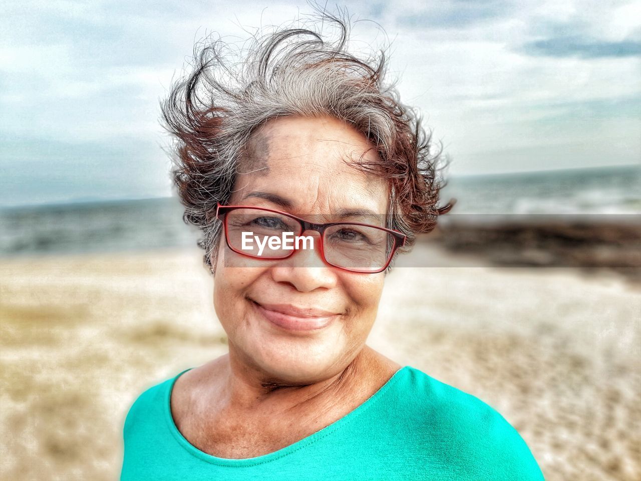 Close-up portrait of smiling senior woman wearing eyeglasses at beach