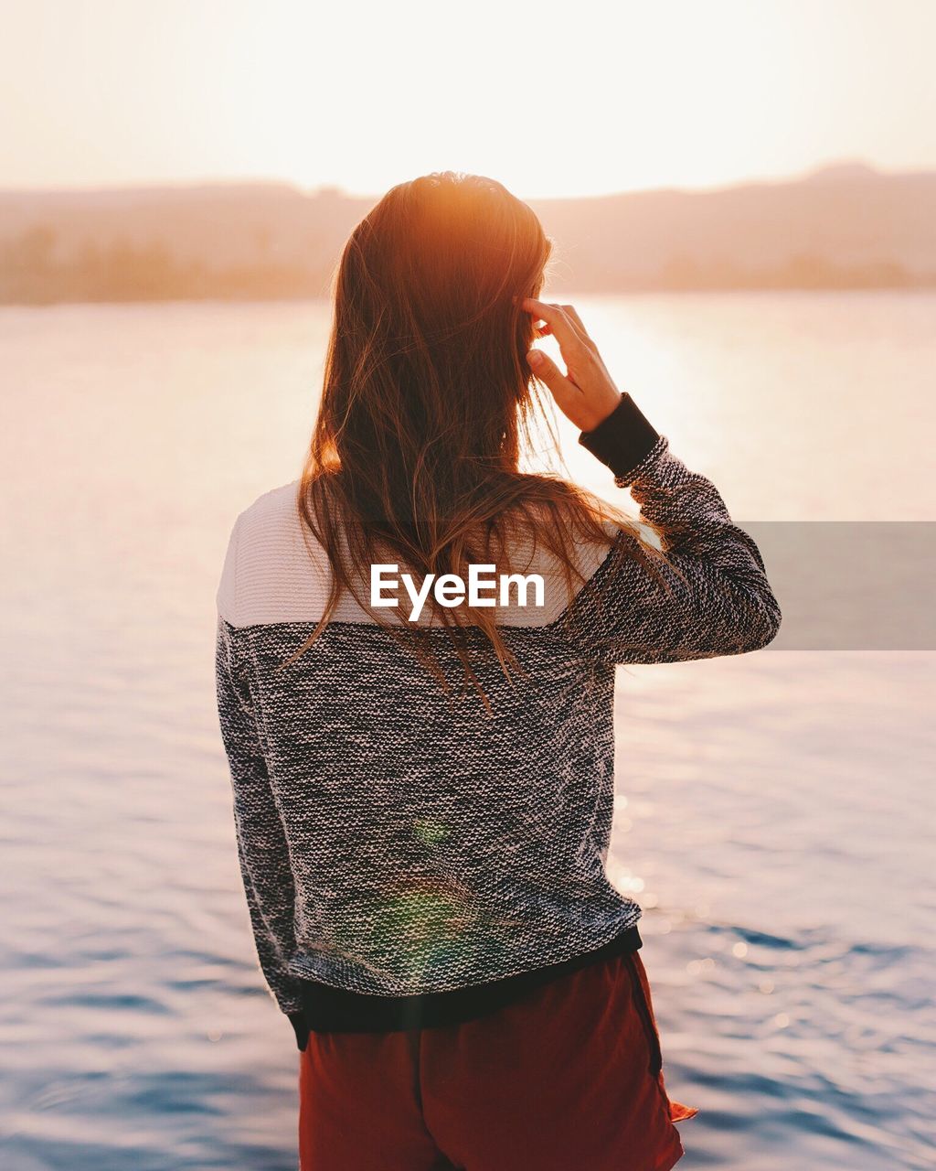 Rear view of woman standing at beach during sunset