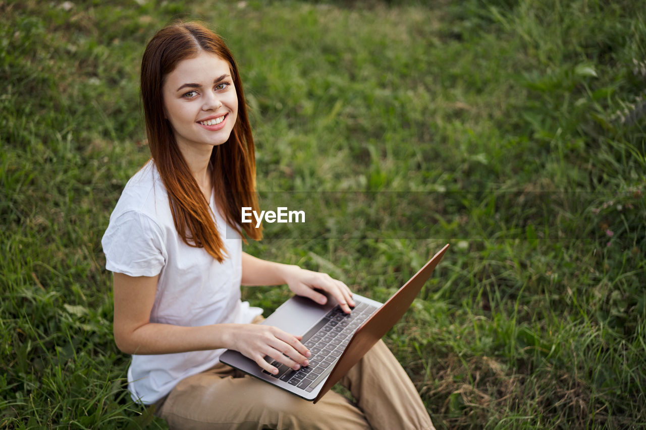 young woman using laptop while sitting on grassy field