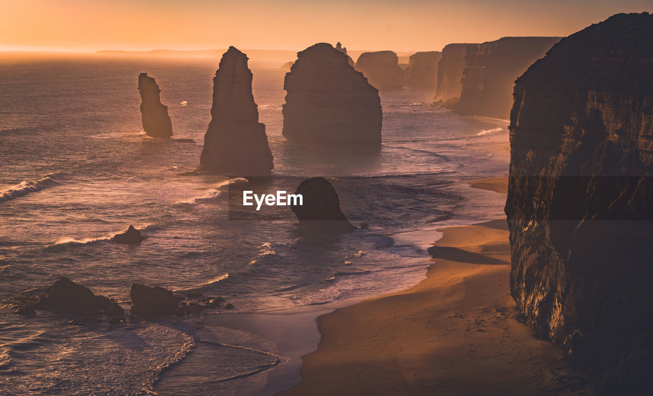 ROCK FORMATIONS AT SHORE AGAINST SKY DURING SUNSET