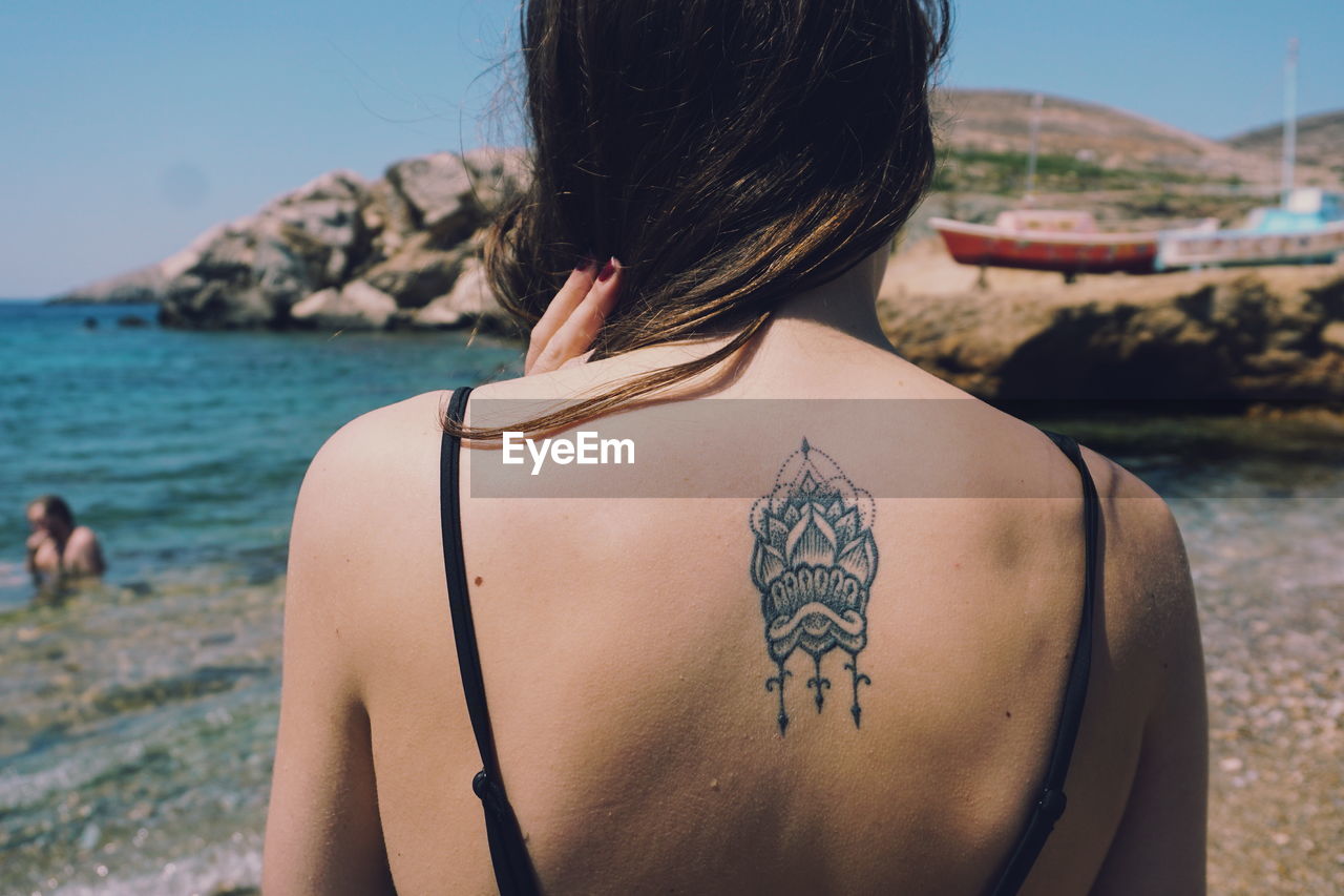 Rear view of woman showing tattoo while standing at beach