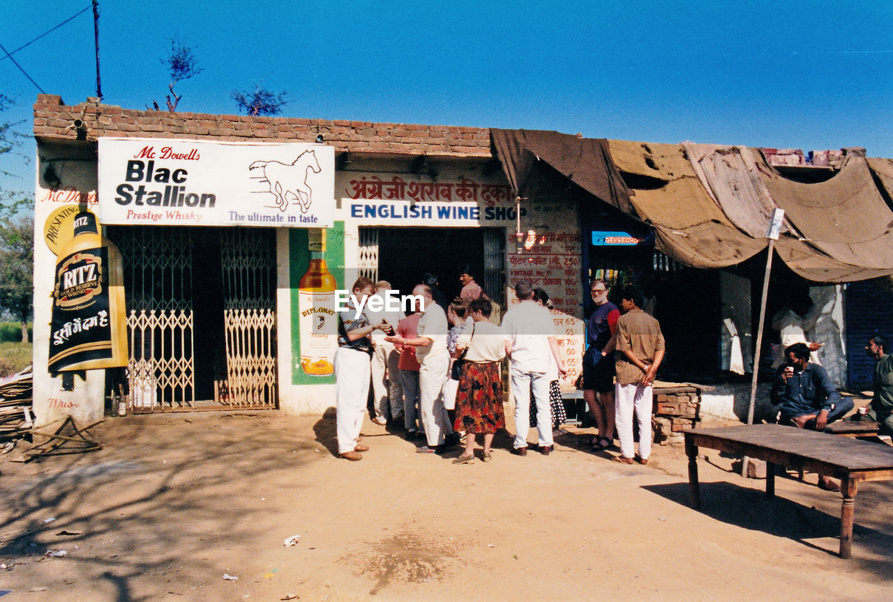 PEOPLE ON STREET AMIDST HOUSES AGAINST CLEAR SKY