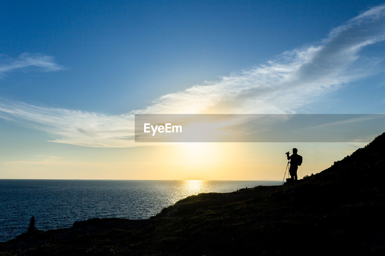 Silhouette of a nature photographer framing a shot, taking pictures at sunset on the beach