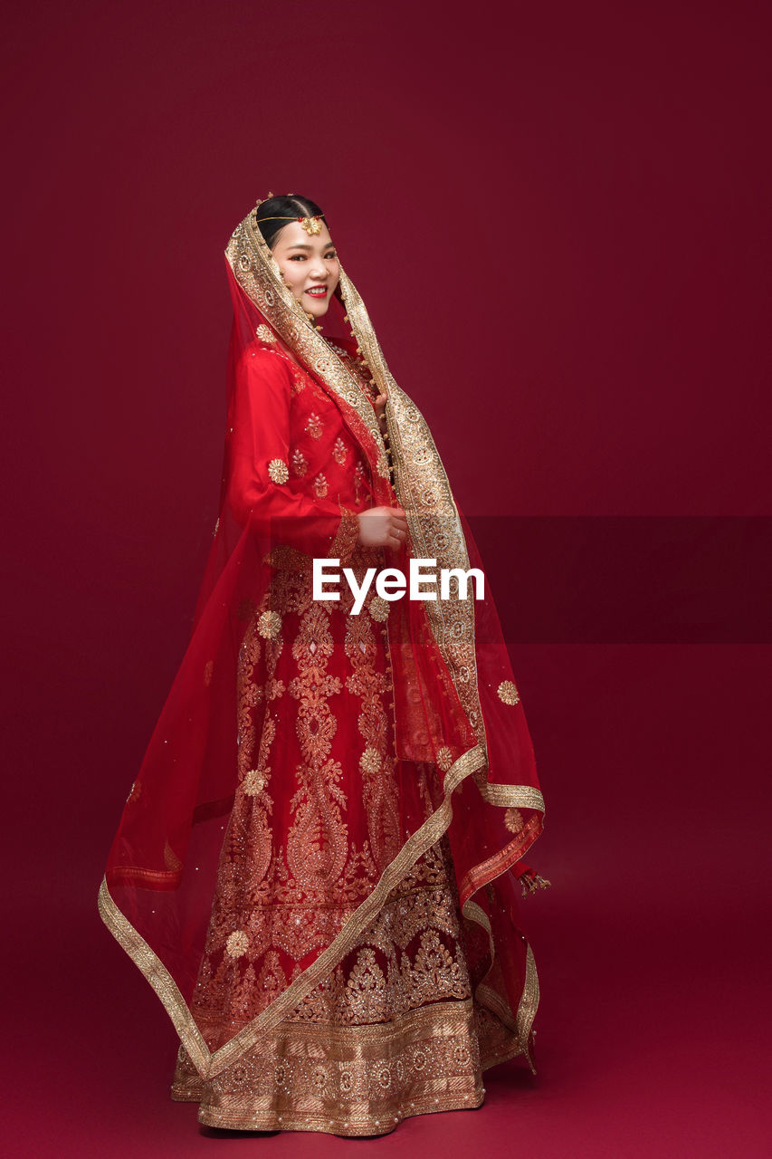 Portrait of smiling in sari standing by red background