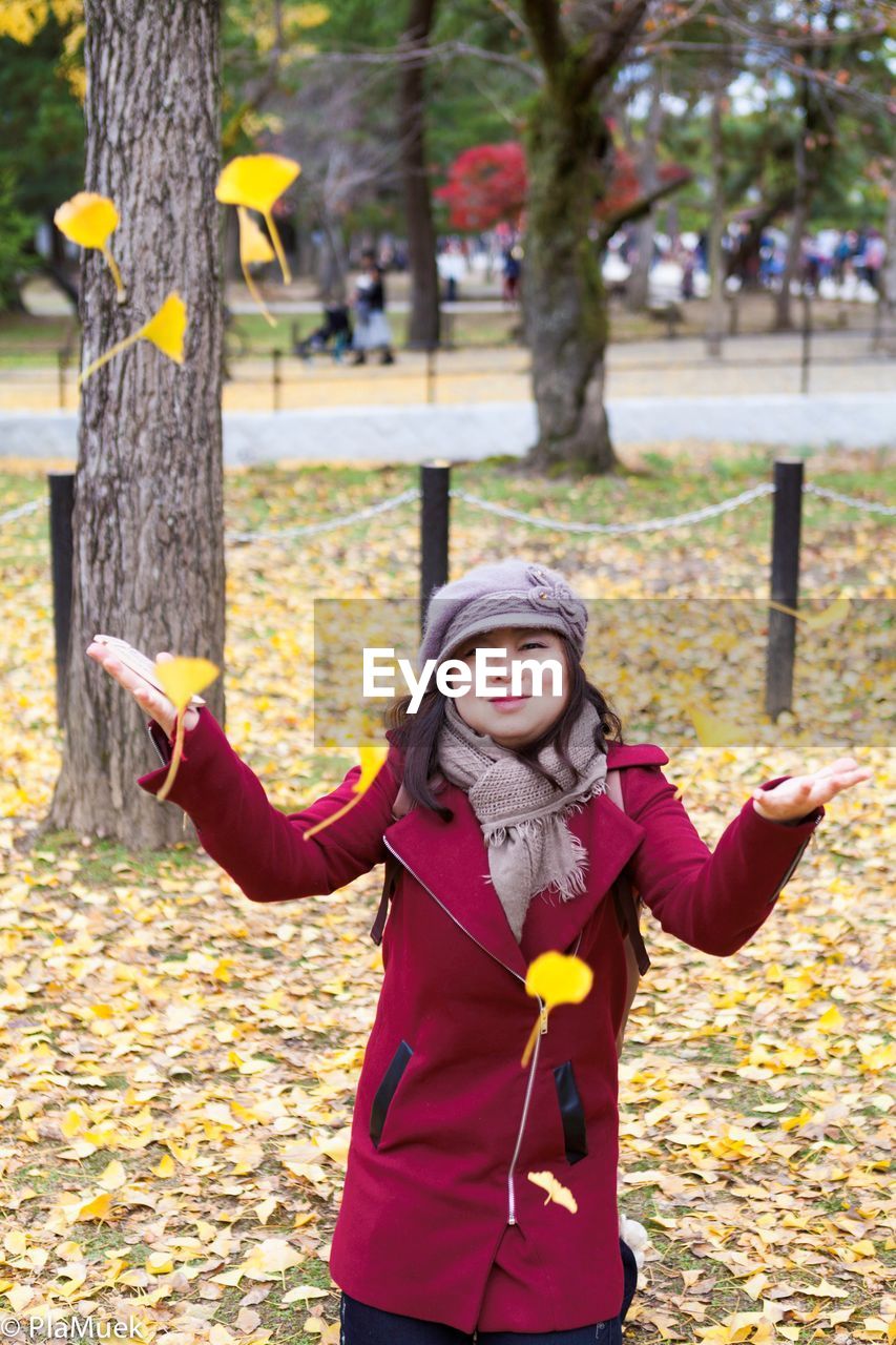 Portrait of woman throwing leaves in park