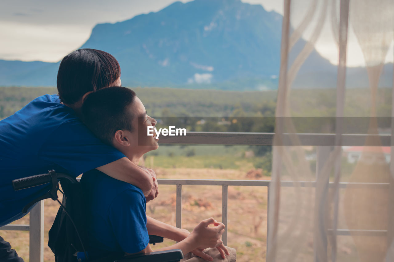 MOTHER AND SON ON RAILING AGAINST MOUNTAINS