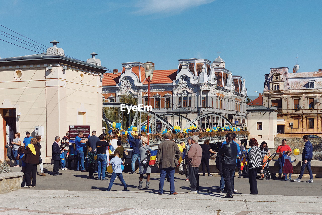 PEOPLE ON STREET BY BUILDINGS AGAINST SKY