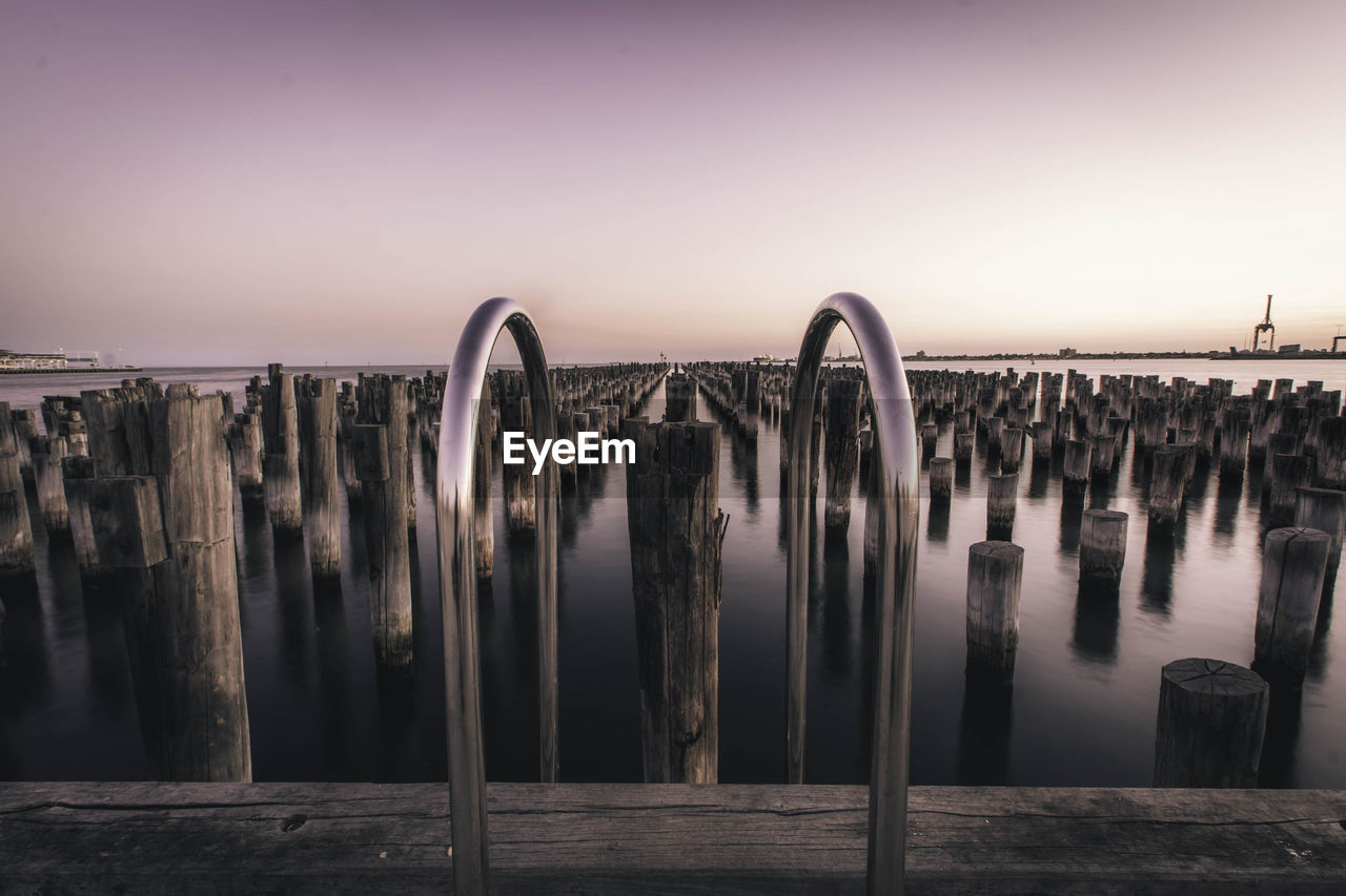 View of wooden posts in sea during sunset