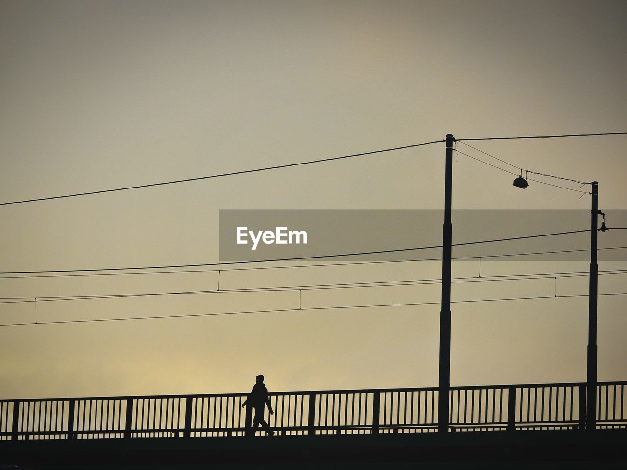 Low angle view of silhouette man walking on bridge against clear sky