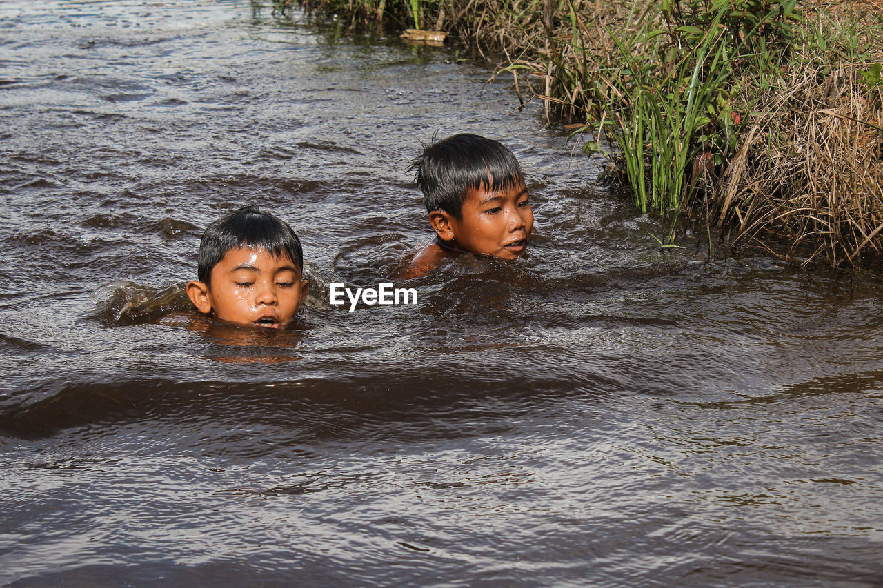 PORTRAIT OF FATHER AND SON IN WATER AT SHORE