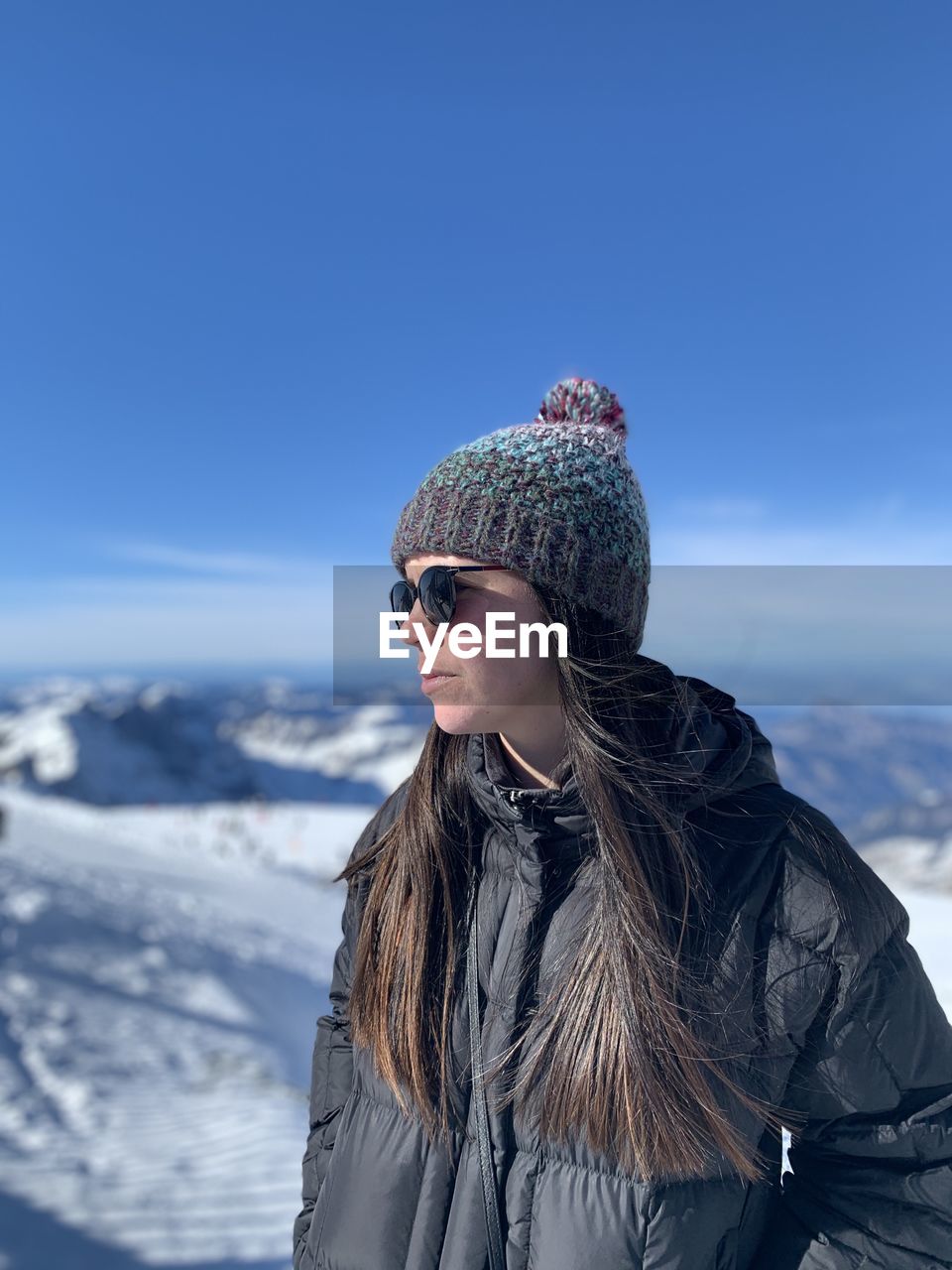 Young woman looking away while standing against sky during winter