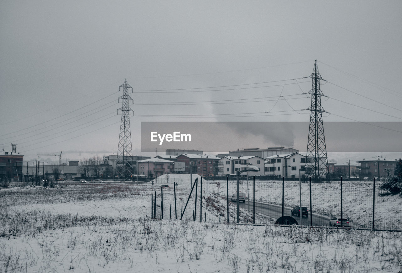 ELECTRICITY PYLONS ON FIELD AGAINST SKY DURING WINTER