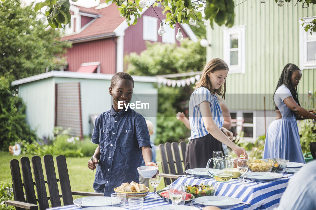 Smiling boy with bowl standing by girl at dining table in backyard party