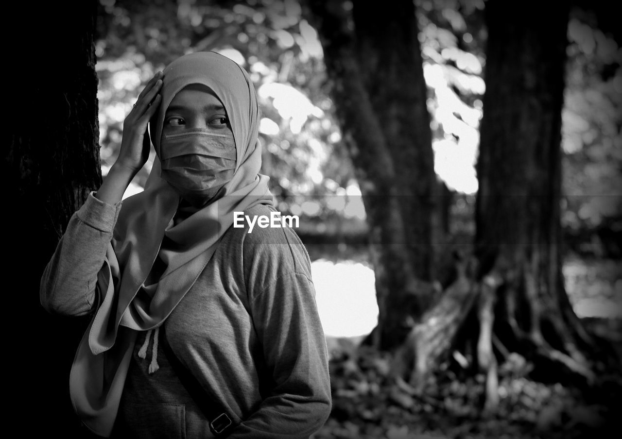 Portrait of young woman standing against tree