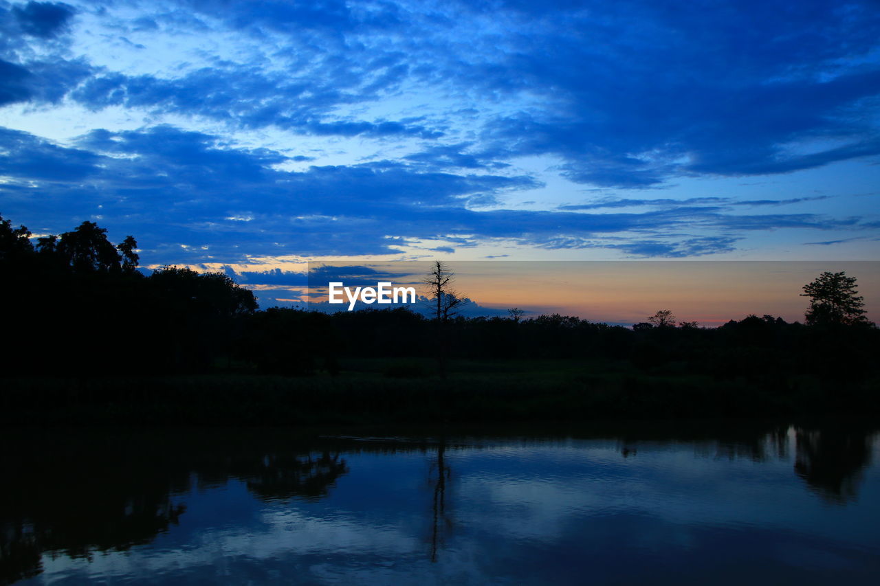 REFLECTION OF SILHOUETTE TREES IN LAKE AGAINST SKY DURING SUNSET