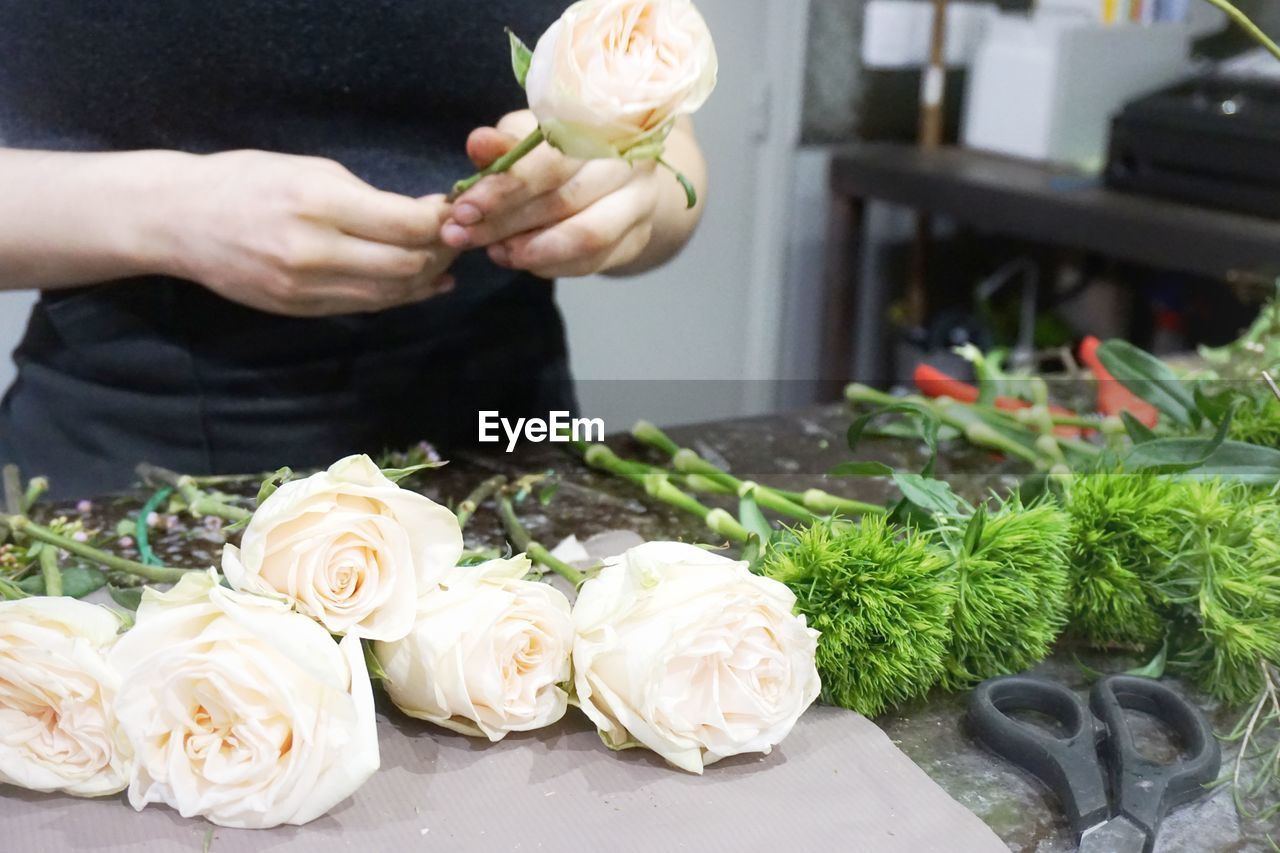 Midsection of florist with white roses at table