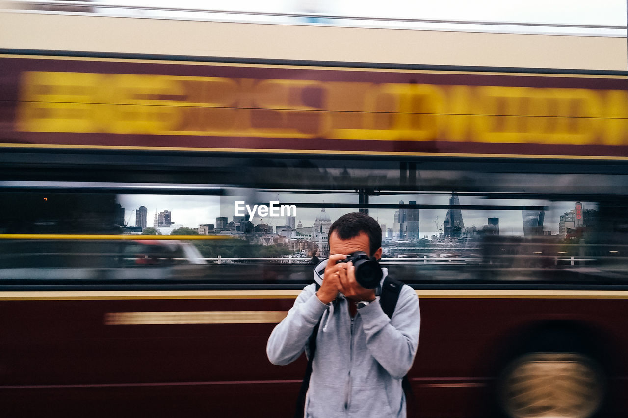 Man photographing against blurred motion of bus in city