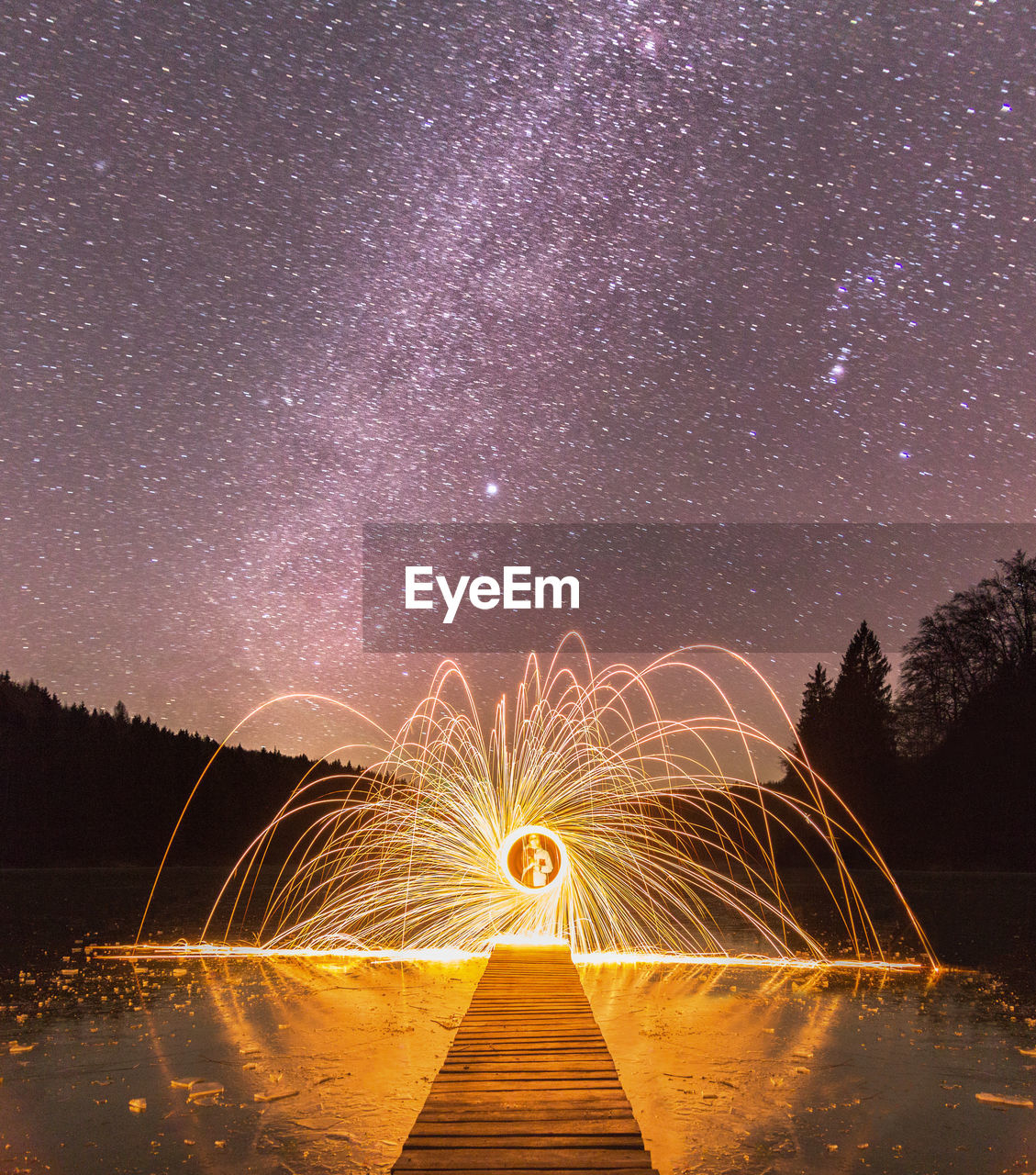 Wire wool on jetty over lake against starry sky