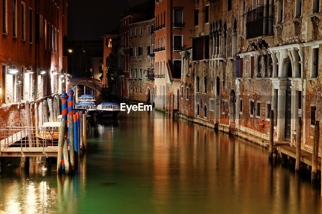 BOATS MOORED IN CANAL BY BUILDINGS IN CITY AT NIGHT