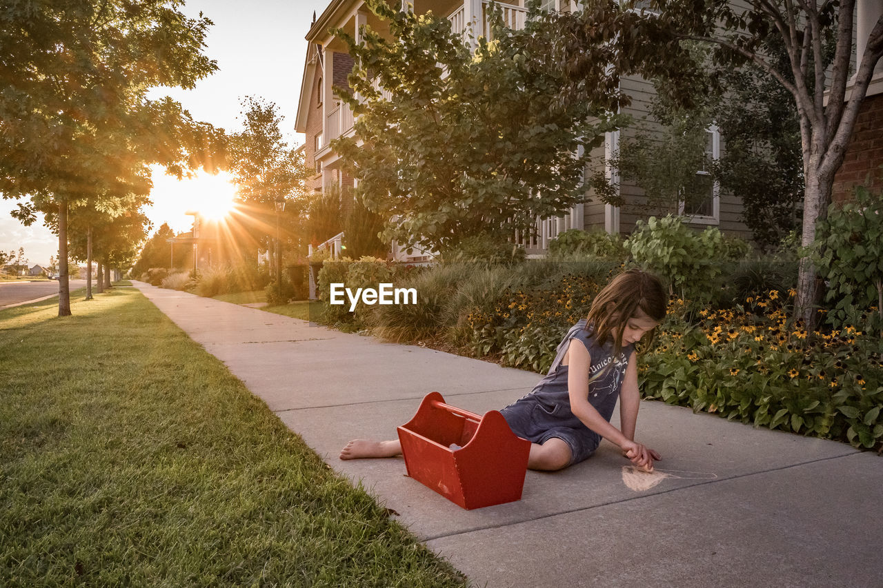 Young girl draws with sidewalk chalk in front of house at sunset